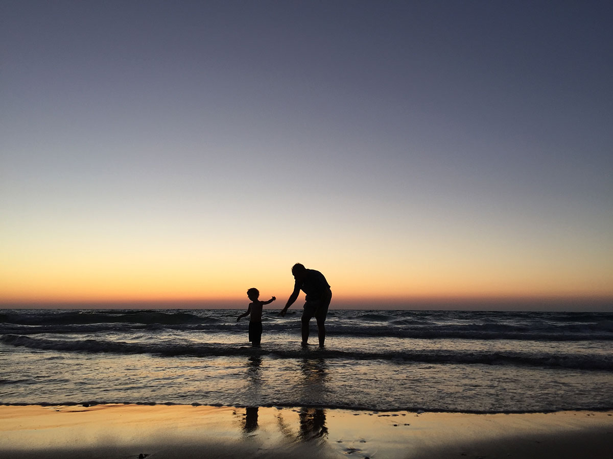 Father and child at ocean during sunset